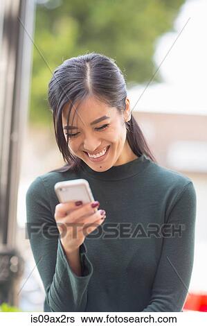 Stock Photograph - Woman holding smartphone looking down smiling. Fotosearch
