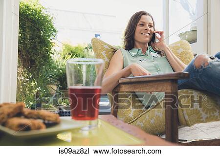 Stock Image - Woman in armchair making telephone call on smartphone. Fotosearch
