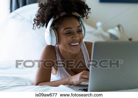 Woman in bedroom, using laptop, wearing headphones View Large Photo Image Stock Photo - Woman in bedroom, using laptop, wearing headphones. Fotosearch
