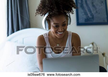 Woman in bedroom, using laptop, wearing headphones View Large Photo Image Stock Photograph - Woman in bedroom, using laptop, wearing headphones. Fotosearch