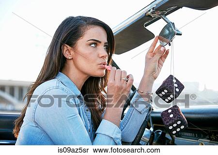 Stock Photography - Woman in convertible car applying lipstick in rear view mirror, Los Angeles, California, USA. Fotosearch