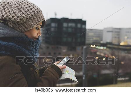 Stock Photography - Woman in knit hat looking at smartphone in city at dusk. Fotosearch