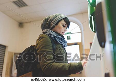 Stock Photo - Woman in knit hat using touchscreen on railway ticket machine. Fotosearch