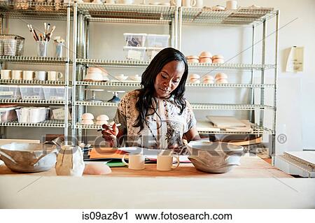 Stock Image - Woman in pottery workshop doing paperwork. Fotosearch