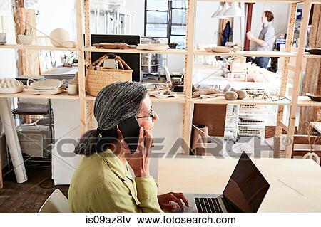 Woman in workshop using phone and laptop View Large Photo Image Stock Photo - Woman in workshop using phone and laptop. Fotosearch