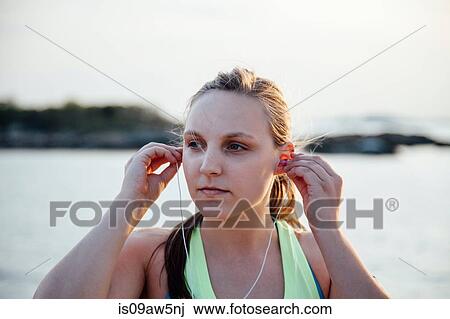 Stock Image - Woman inserting earbuds looking away. Fotosearch