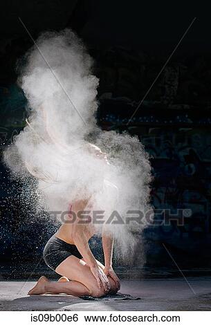 Stock Photograph - Woman kneeling throwing powder covered hair back. Fotosearch
