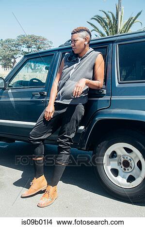 Picture - Woman leaning against car looking away. Fotosearch