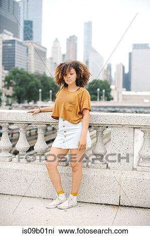 Stock Image - Woman leaning against stone baluster in front of Chicago skyline, Illinois. Fotosearch