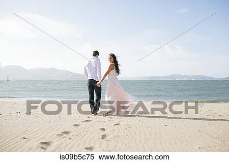 Woman looking back while strolling hand in hand with boyfriend on beach View Large Photo Image Stock Photography - Woman looking back while strolling hand in hand with boyfriend on beach. Fotosearch