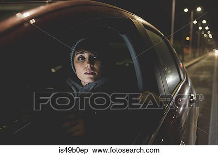 Stock Photography - Woman looking out of car window on city roadside at night. Fotosearch