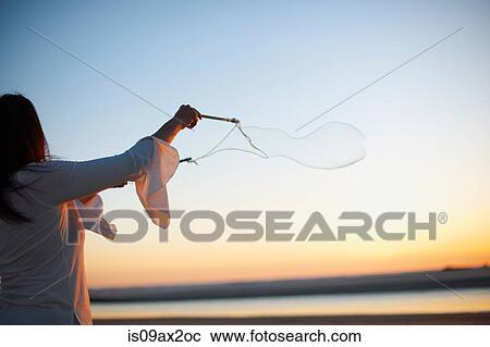 Stock Image - Woman making bubbles on Cannon Beach at sunset, California, USA. Fotosearch