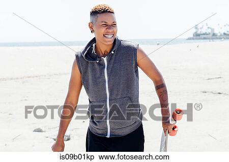 Woman on beach carrying skateboard smiling View Large Photo Image Stock Photography - Woman on beach carrying skateboard smiling. Fotosearch