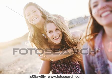 Woman on beach giving friend piggyback looking at camera smiling View Large Photo Image Stock Photo - Woman on beach giving friend piggyback looking at camera smiling. Fotosearch