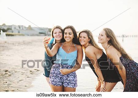 Stock Photo - Woman on beach using smartphone to take selfie smiling. Fotosearch