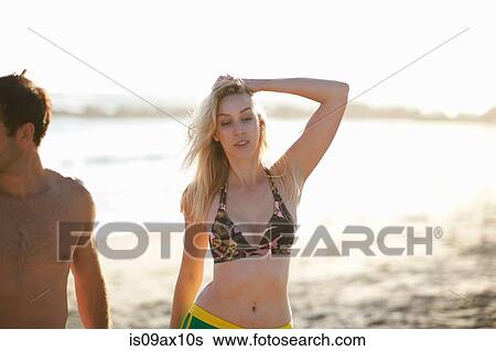 Stock Photograph - Woman on beach wearing bikini top, hand in hair looking down. Fotosearch