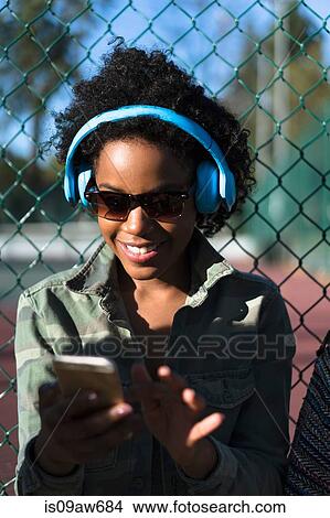 Woman outdoors, wearing headphones, using smartphone View Large Photo Image Picture - Woman outdoors, wearing headphones, using smartphone. Fotosearch