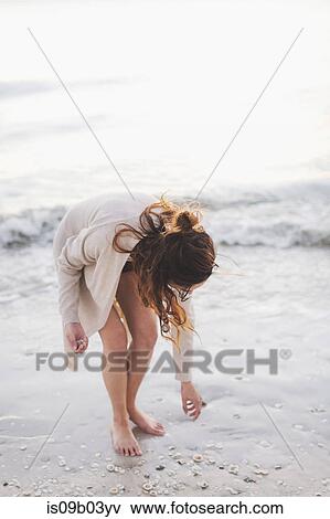 Stock Photo - Woman picking seashells on beach. Fotosearch