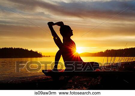 Picture - Woman practising yoga by lake at sunset. Fotosearch