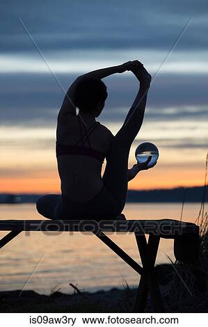 Stock Photo - Woman practising yoga by lake at sunset. Fotosearch