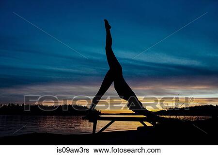 Stock Photograph - Woman practising yoga by lake at sunset. Fotosearch