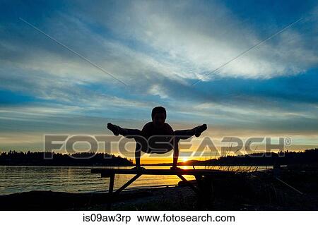 Stock Photography - Woman practising yoga by lake at sunset. Fotosearch