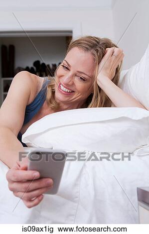 Woman reading smartphone texts in bed View Large Photo Image Stock Image - Woman reading smartphone texts in bed. Fotosearch