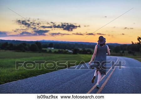 Stock Photo - Woman running down rural road at sunset. Fotosearch