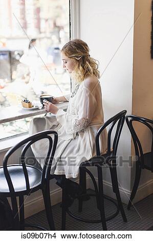 Woman sitting at window seat in coffee shop View Large Photo Image Picture - Woman sitting at window seat in coffee shop. Fotosearch