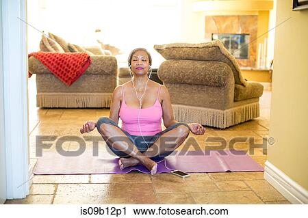 Stock Image - Woman sitting cross legged meditating. Fotosearch