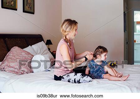 Woman sitting on bed plaiting toddler daughter's hair View Large Photo Image Stock Photography - Woman sitting on bed plaiting toddler daughter's hair. Fotosearch