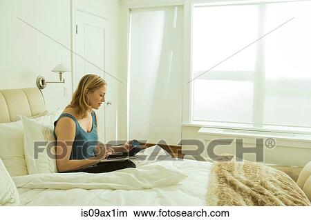 Woman sitting on bed reading update on digital tablet View Large Photo Image Picture - Woman sitting on bed reading update on digital tablet. Fotosearch