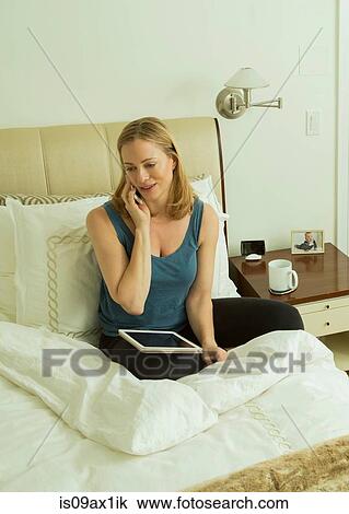 Woman sitting on bed talking on smartphone View Large Photo Image Stock Image - Woman sitting on bed talking on smartphone. Fotosearch