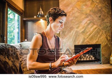 Stock Photography - Woman sitting on sofa reading digital tablet. Fotosearch
