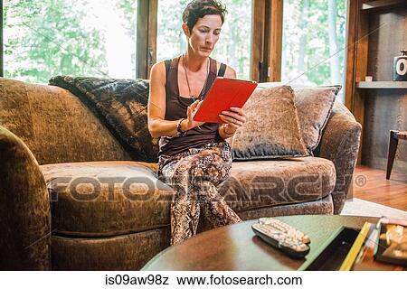 Woman sitting on sofa using digital tablet touchscreen View Large Photo Image Stock Photo - Woman sitting on sofa using digital tablet touchscreen. Fotosearch