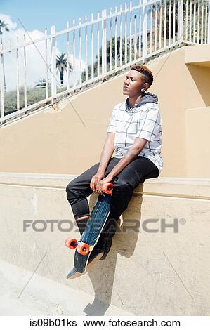 Woman sitting on wall holding skateboard, eyes closed View Large Photo Image Stock Photograph - Woman sitting on wall holding skateboard, eyes closed. Fotosearch