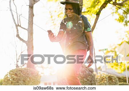 Stock Photograph - Woman skateboarding on pavement, looking at smartphone. Fotosearch