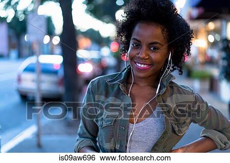 Woman standing in street, wearing earphones, smiling View Large Photo Image Stock Photograph - Woman standing in street, wearing earphones, smiling. Fotosearch