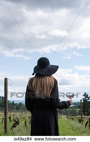 Picture - Woman standing in vineyard, holding glass of wine, rear view. Fotosearch