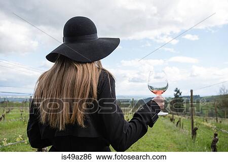 Woman standing in vineyard, holding glass of wine, rear view View Large Photo Image Stock Photograph - Woman standing in vineyard, holding glass of wine, rear view. Fotosearch