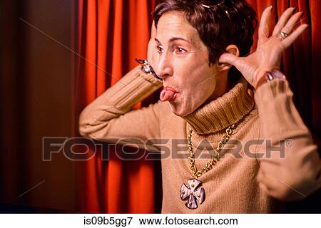 Stock Photo - Woman sticking out tongue, red curtain background. Fotosearch