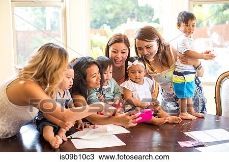 Stock Image - Woman taking selfie with mothers and babies at dining table. Fotosearch