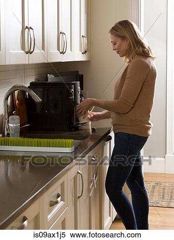Stock Photography - Woman using coffee machine in kitchen. Fotosearch