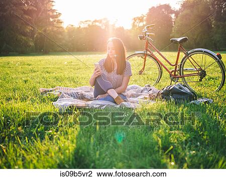 Stock Image - Woman using mobile phone on grass. Fotosearch