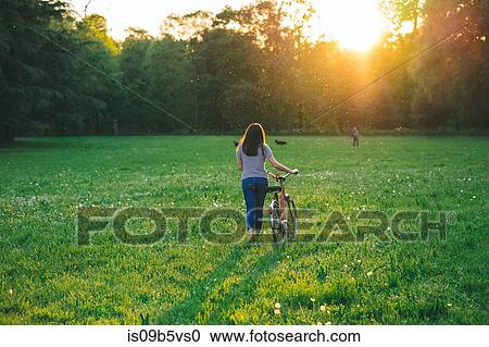 Stock Image - Woman walking bicycle on grass. Fotosearch