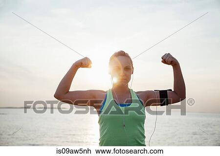 Woman wearing activity tracker, arms raised flexing muscles looking at camera View Large Photo Image Stock Image - Woman wearing activity tracker, arms raised flexing muscles looking at camera. Fotosearch