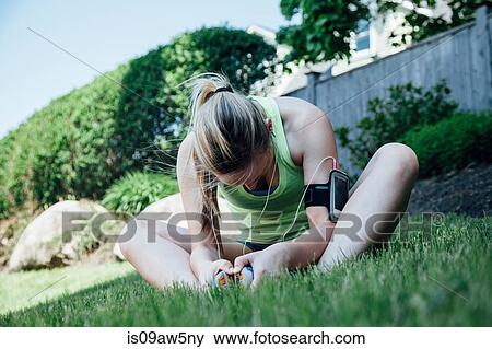 Woman wearing activity tracker sitting on grass stretching looking down View Large Photo Image Stock Photo - Woman wearing activity tracker sitting on grass stretching looking down. Fotosearch