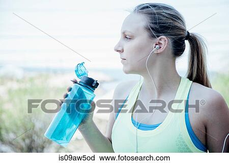 Woman wearing earbuds holding plastic water bottle looking away View Large Photo Image Stock Image - Woman wearing earbuds holding plastic water bottle looking away. Fotosearch