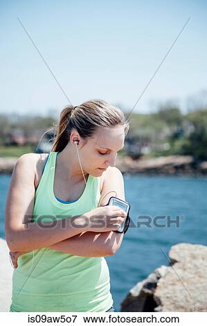 Woman wearing earbuds looking at activity tracker on arm View Large Photo Image Stock Photo - Woman wearing earbuds looking at activity tracker on arm. Fotosearch