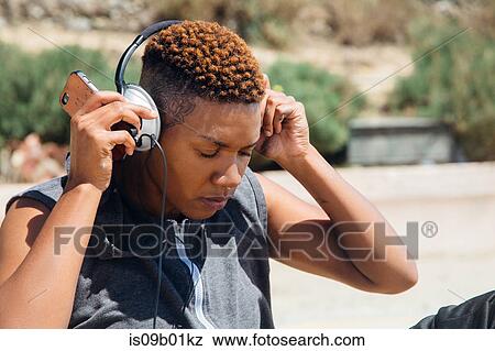 Woman wearing headphones holding smartphone looking down View Large Photo Image Stock Photo - Woman wearing headphones holding smartphone looking down. Fotosearch